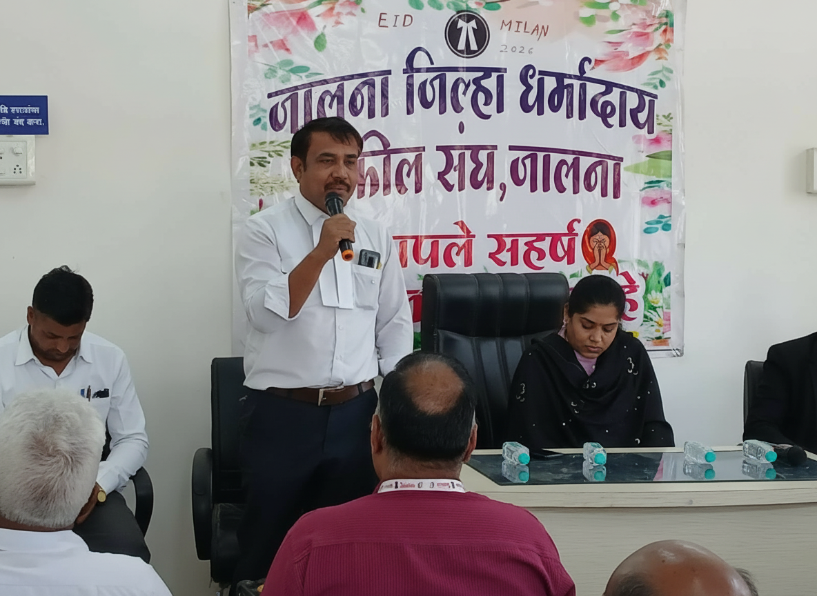 Community meeting with public speaker - NewsNation Online A man speaking into a microphone at a meeting with several seated attendees and a banner in Hindi behind him