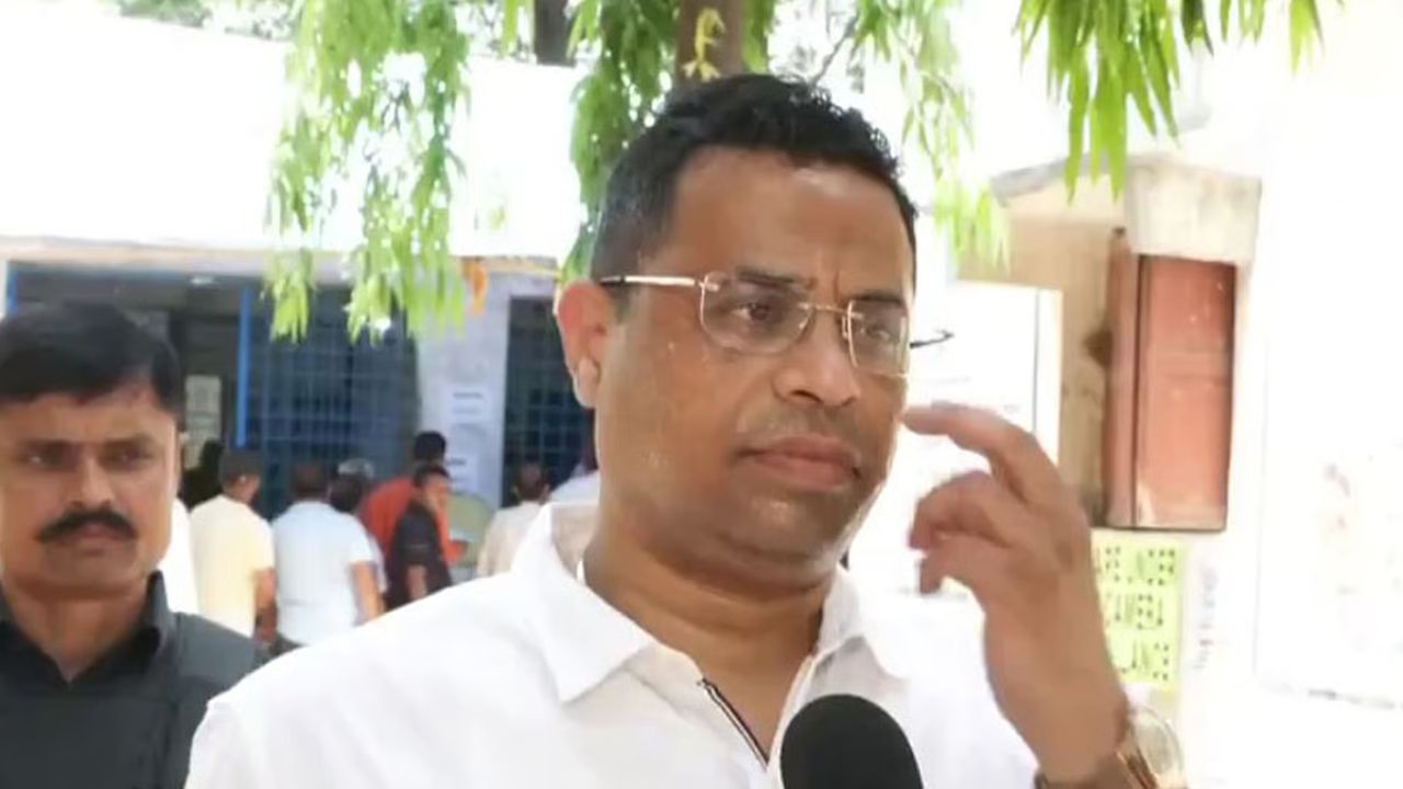 Man in a white shirt being interviewed outdoors, holding a microphone, with onlookers in the background.