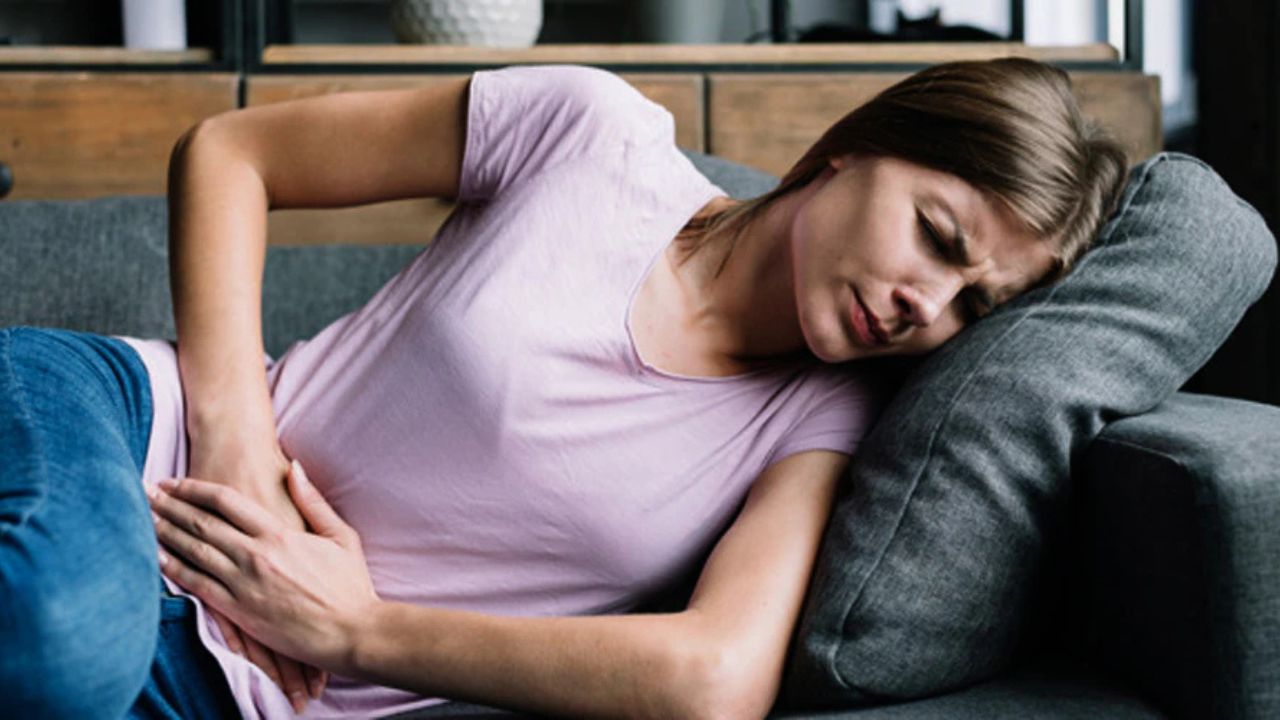 Woman lying on a sofa, clutching her stomach in visible abdominal pain.