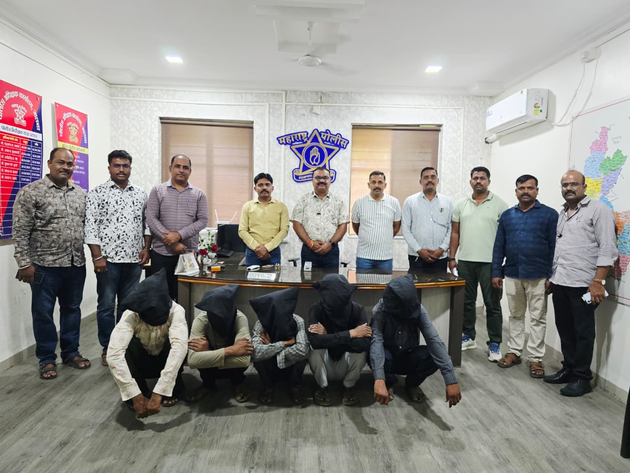 WhatsApp Image 2026-07-18 at 61502 PM - NewsNation Online Ten men stand behind a desk in an office, while five individuals kneel in front with black hoods over their heads; maps and posters adorn the walls.