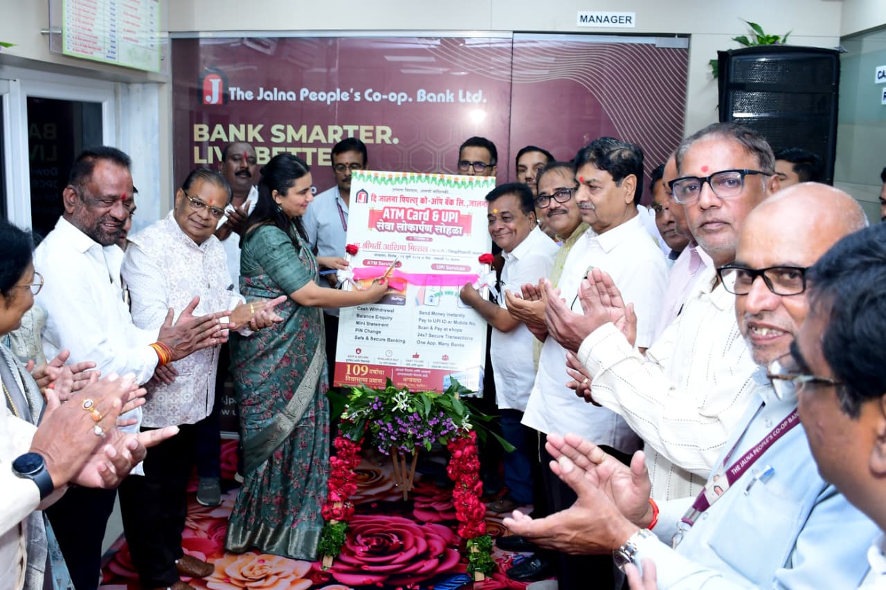 Group of professionals at a bank ceremony unveiling a poster, with a flower-strewn pedestal in front.