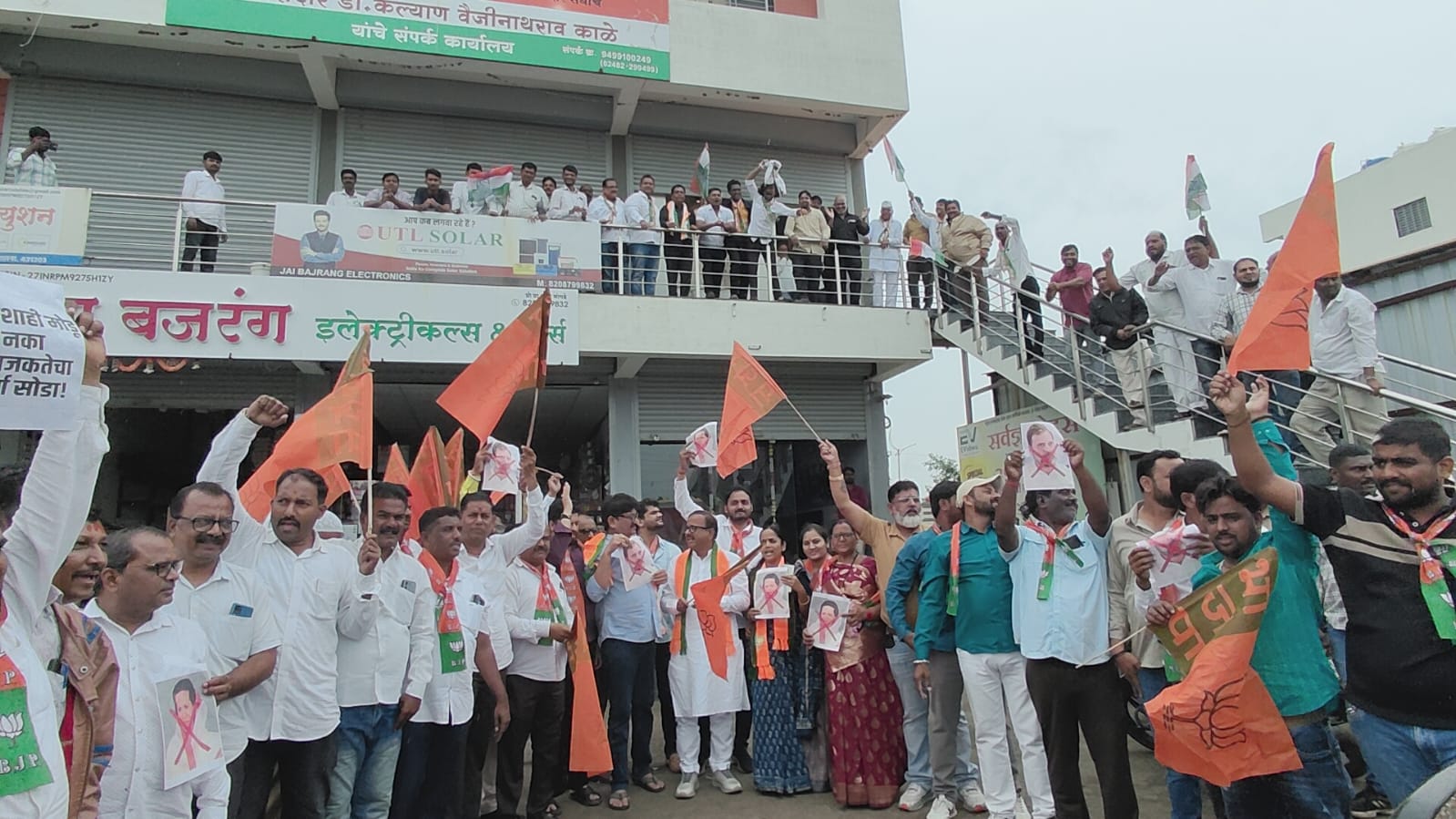 Crowd of protesters in white and colorful clothes marching with orange flags and posters bearing a woman's portrait outside a storefront building.