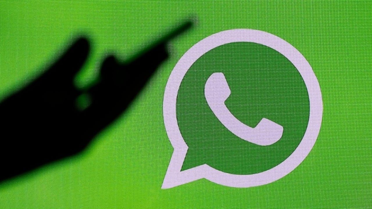 Dark hand silhouette reaching toward the white WhatsApp logo on a bright green background