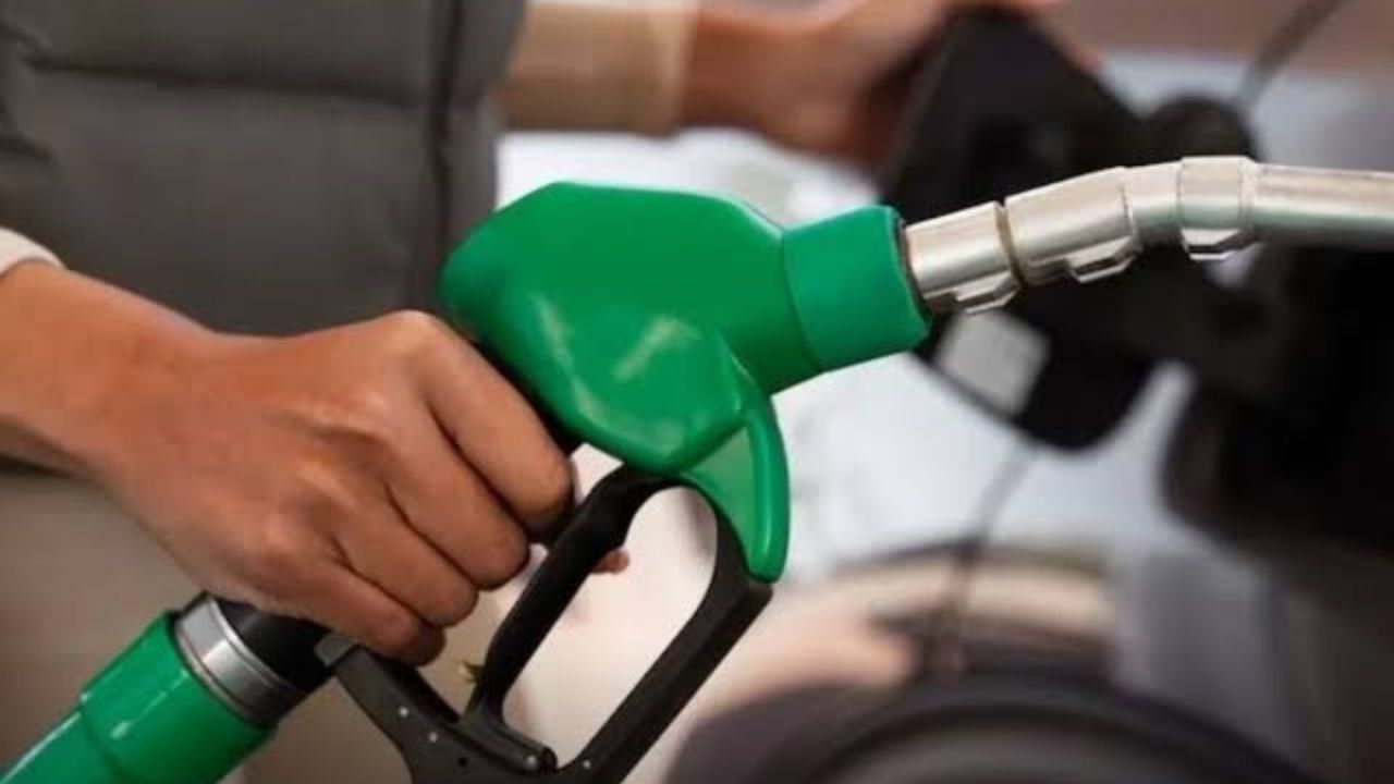 Person gripping a green gas pump nozzle as they refuel a vehicle at a gas station.