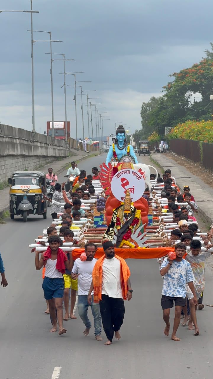 Large parade on a city road carrying a decorated chariot with a blue-skinned deity statue atop, crowds of people walking beside and guiding the float.