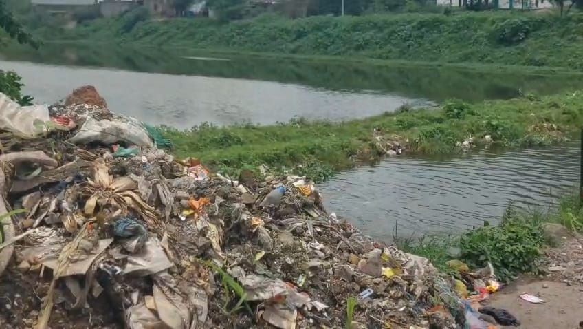 IMG-20260804-WA0029 - NewsNation Online Pile of garbage and plastic waste piled beside a river, with green vegetation in the background.