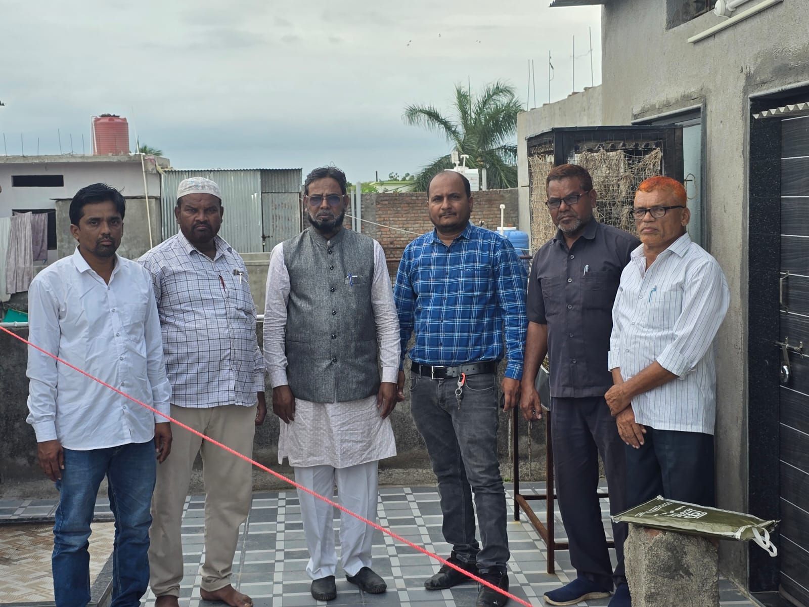 Seven men stand on a tiled rooftop terrace, posing for a group photo outdoors in casual to traditional attire.