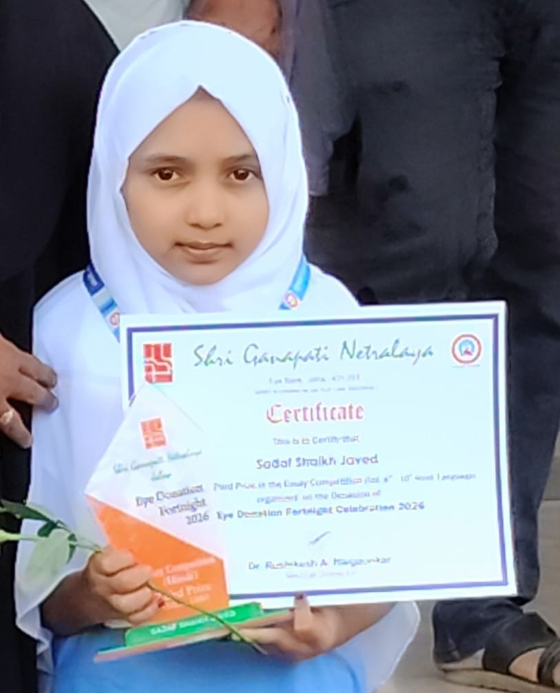 Young girl wearing a white hijab and light blue outfit holds a certificate and a rose at an award ceremony, looking at the camera.