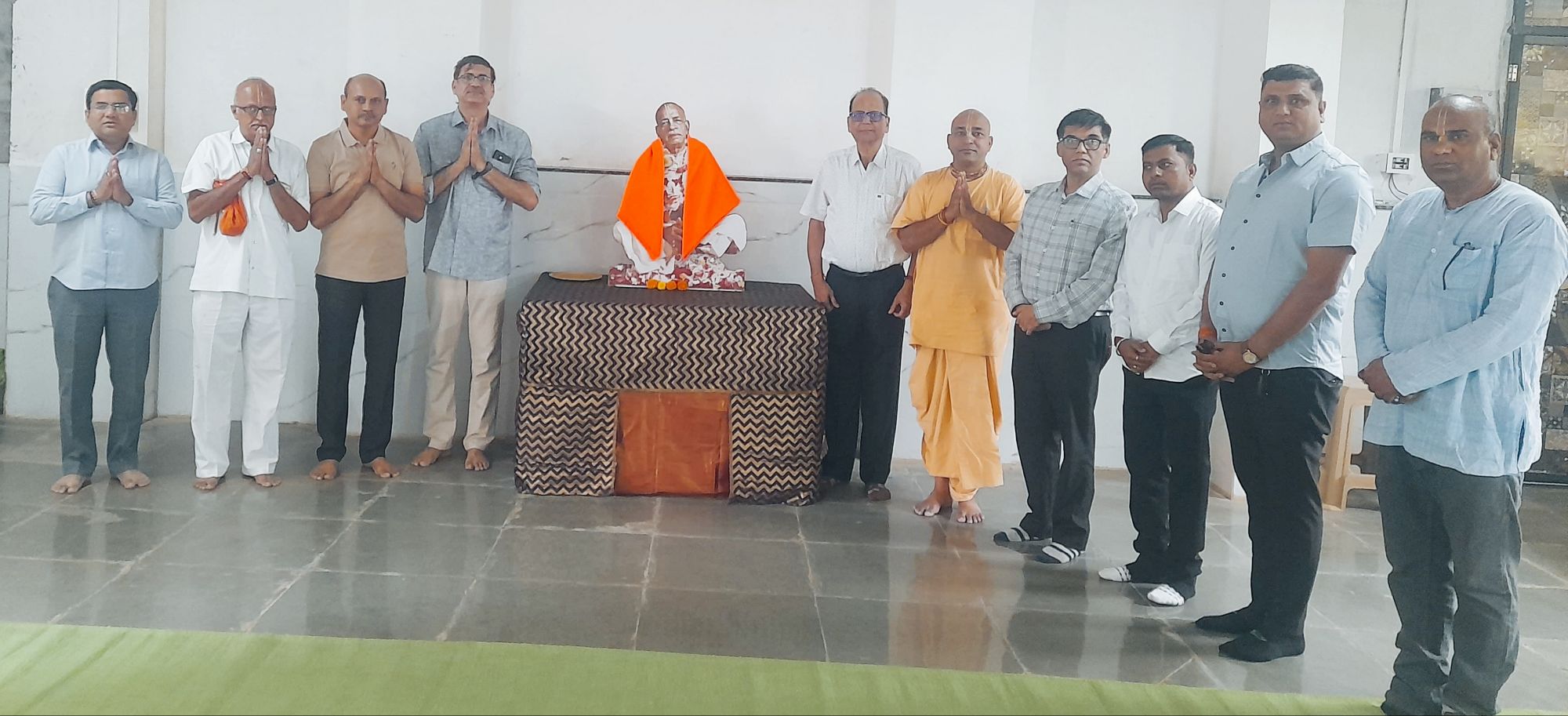 img-20260902-wa0023(1)1171363251848923652 - NewsNation Online Group of men standing in a row with hands folded in prayer around a small shrine, where a statue draped in an orange cloth sits on a decorated table.
