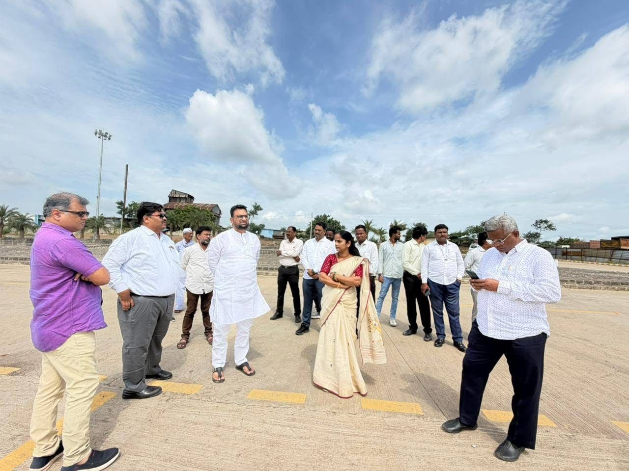 img-20260903-wa00034879822457569586922 - NewsNation Online Group of professionals standing on a wide paved outdoor area, a woman in a cream sari among white shirts, some people looking at a phone; blue sky with clouds above.
