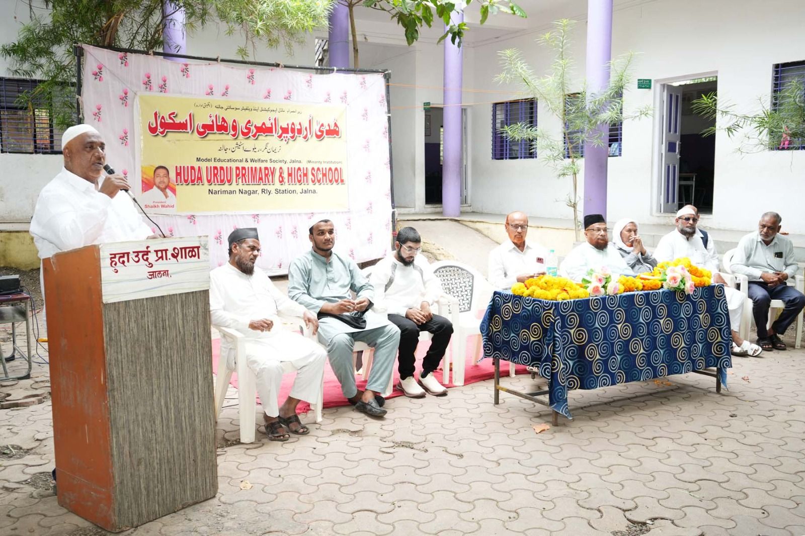 img-20260904-wa00397703139063054691818 - NewsNation Online Senior man in white attire speaks at a podium during a school event; banner behind him reads Huda Urdu Primary & High School, Jalna.