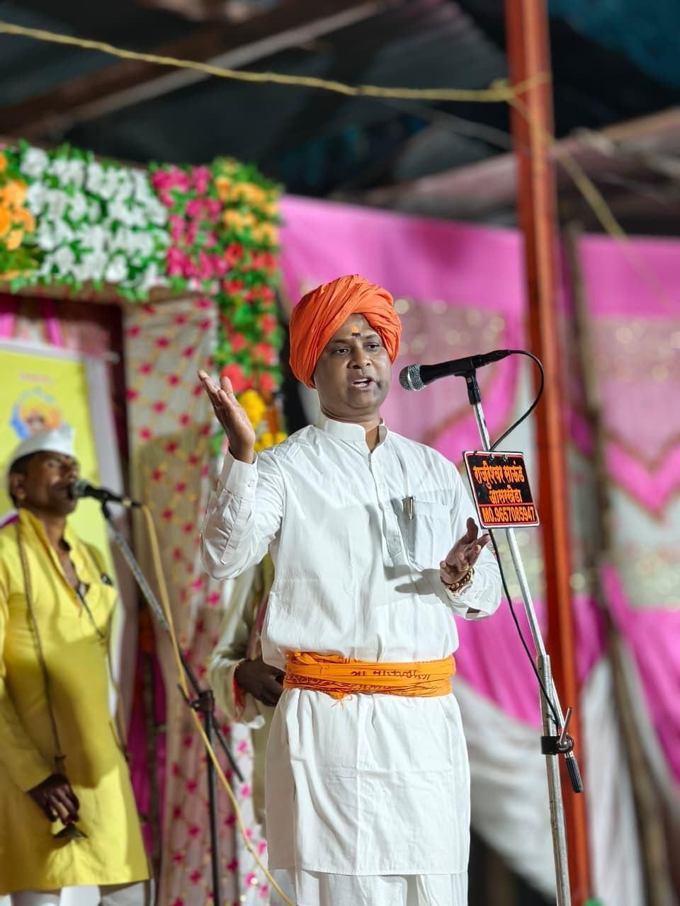 img-20260906-wa00198715409647031082951 - NewsNation Online Man in white traditional attire and orange turban speaking at a microphone on a decorated stage, gesturing with his hand raised.
