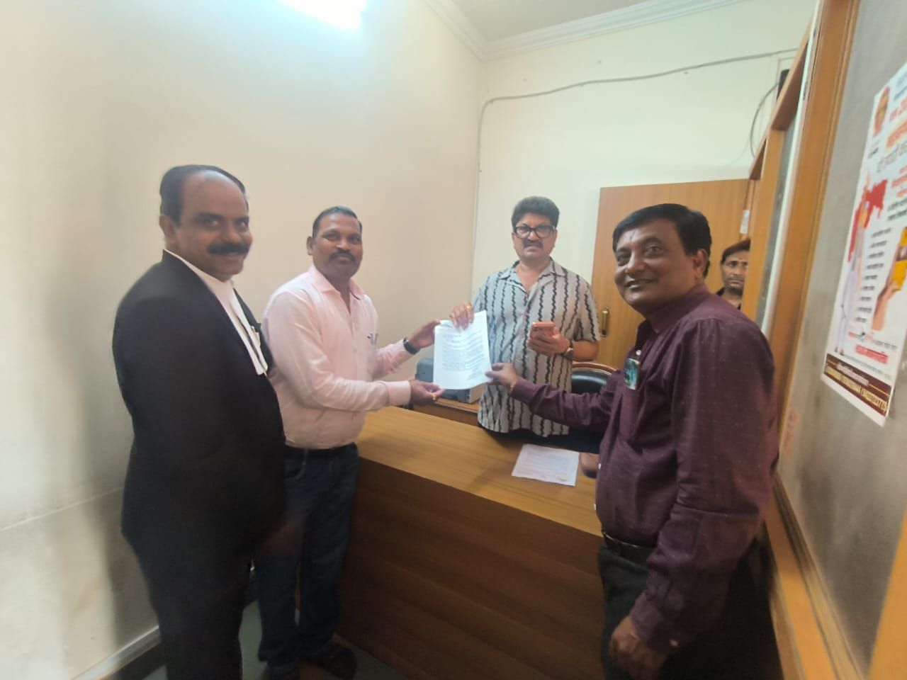 img-20260909-wa00185781697602336731820 - NewsNation Online Four men in an office pass a document over a wooden desk during a small meeting.