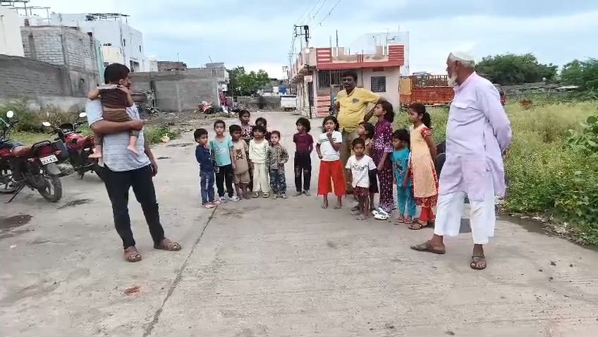 img-20260912-wa00167425779608444218366 - NewsNation Online A man holds a toddler while a group of about 20 children stands in a line on a rural street, with an elder man in white robes observing.
