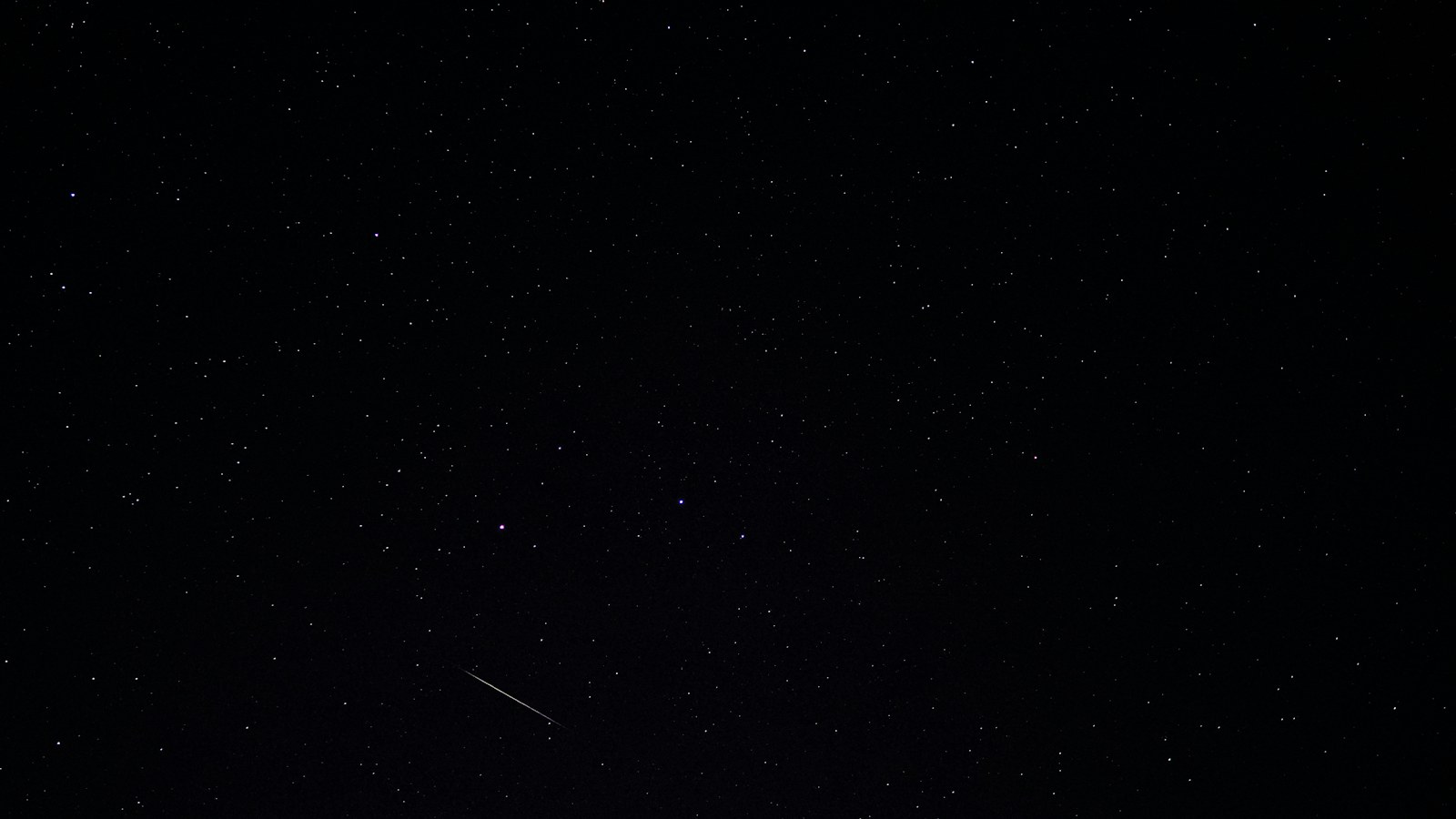 Dark night sky sprinkled with stars and a bright meteor streaking across the lower-left corner.