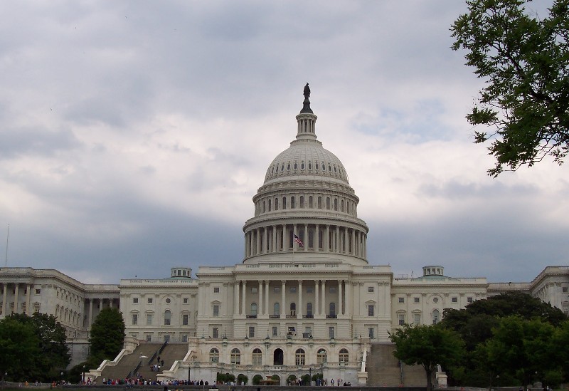 The U.S. Capitol building in Washington, D.C. with a large dome, statue atop, and steps leading to a plaza with visitors nearby.